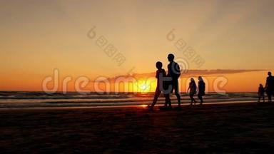 在海浪和红日落的背景下，人们沿着海边散步的剪影。